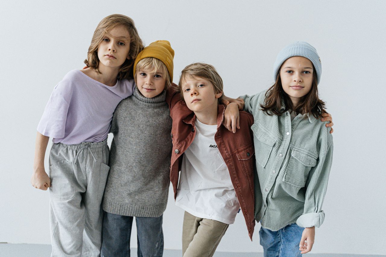 Group of fashionable kids posing in a studio setting wearing trendy outfits.