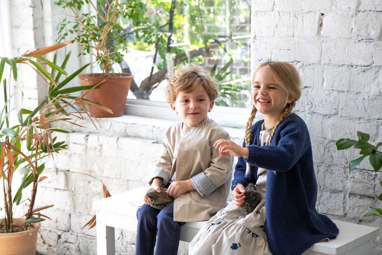 Two joyful kids bonding with adorable chicks indoors surrounded by plants.
